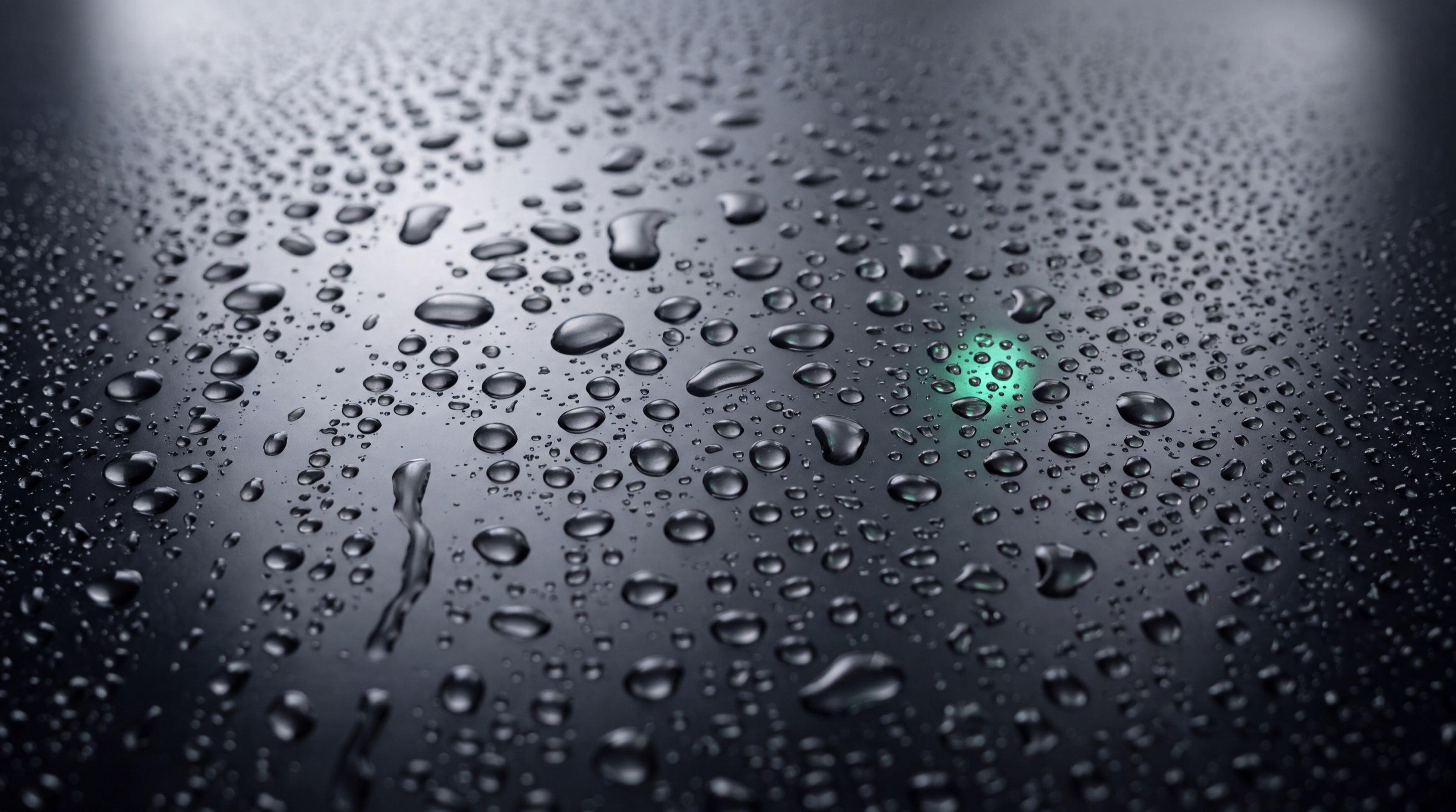 Gouttes d’eau sur une vitre sombre, une lueur verte entre les gouttes.