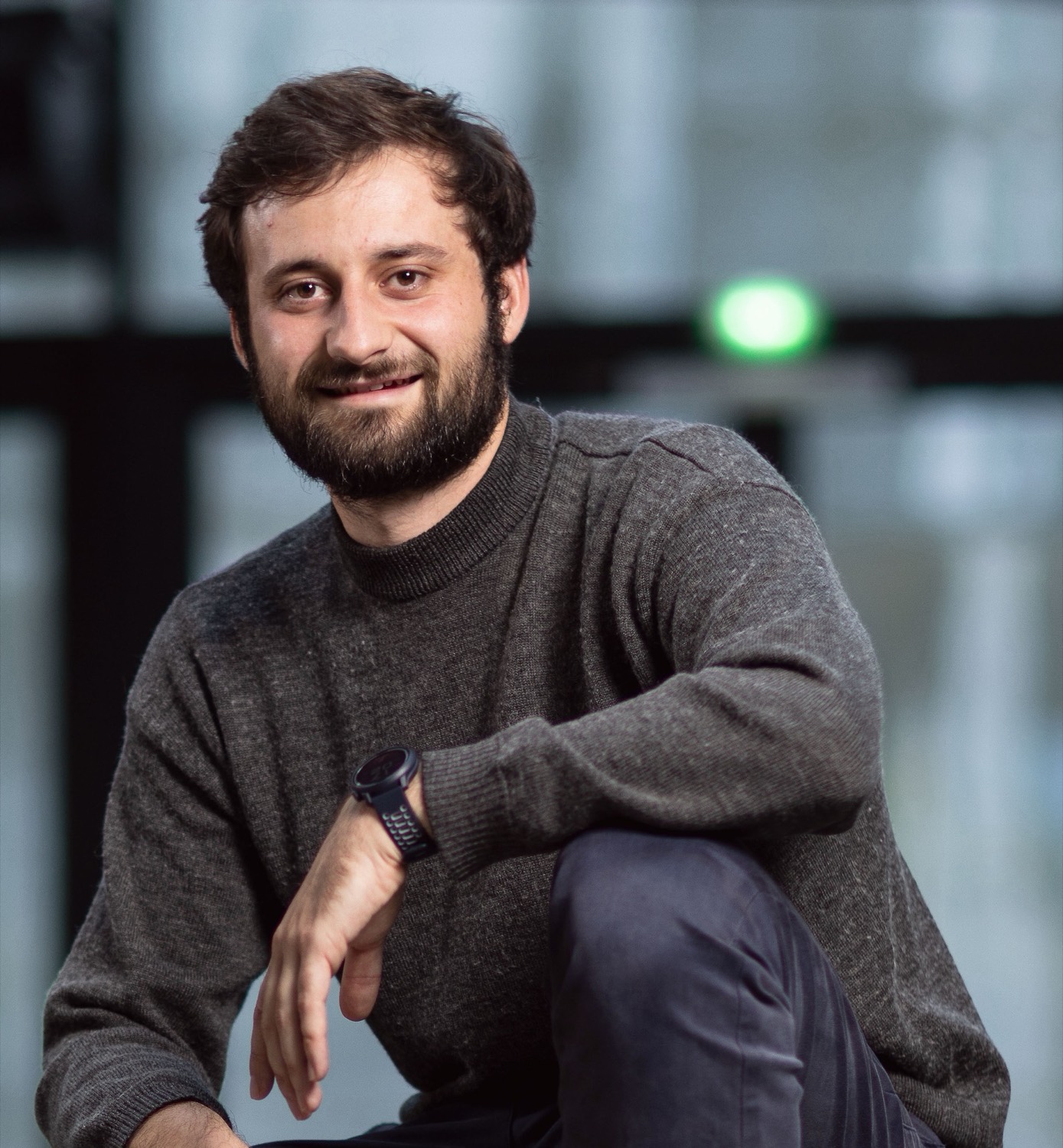 Clément Lemerle, accroupi, pull gris, devant une verrière.
